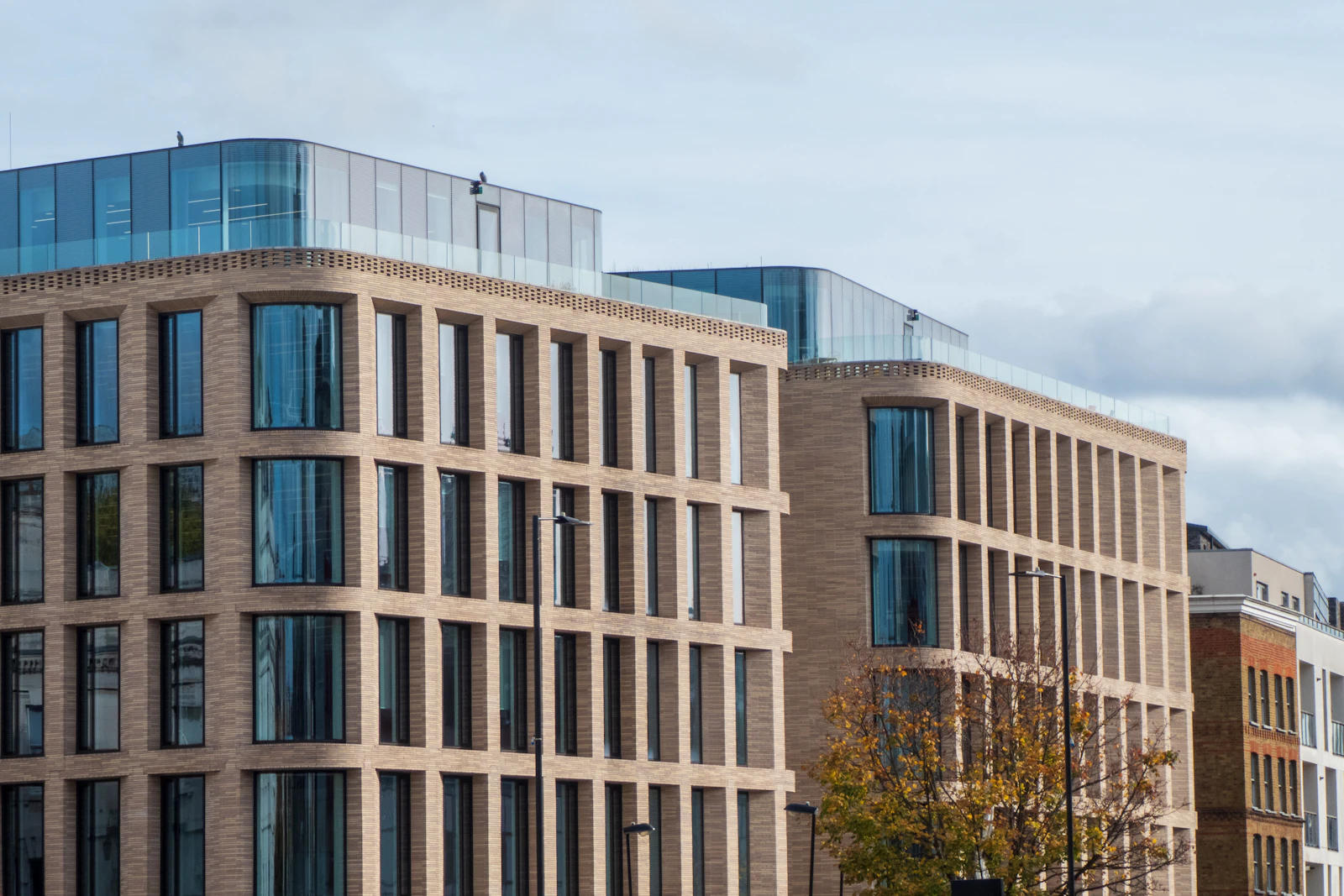 Two brick and glass office buildings of seven floors on a city street, a tree turning in front.