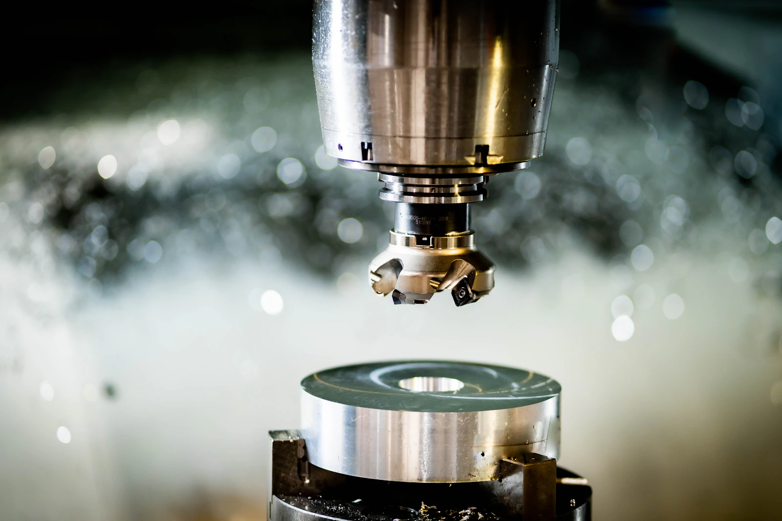 A milling cutter above a round metal blank in a machine shop, coolant mist behind.