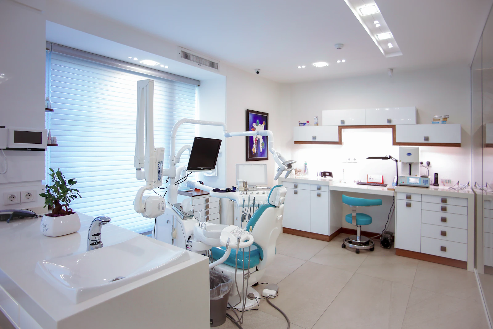 A bright dental surgery with a patient chair, a monitor and wall cabinets.