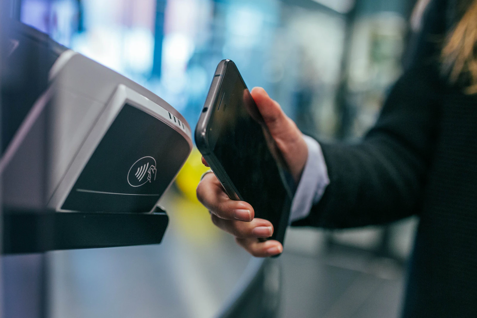 A hand holding a phone to a contactless card terminal.